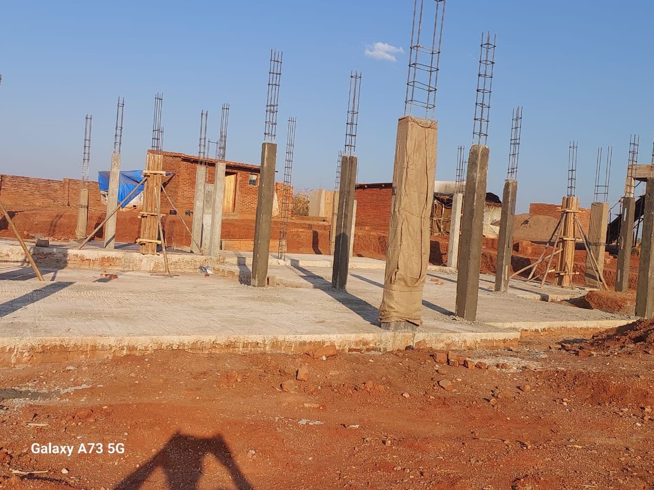 Ground floor slab and column casting. The ground floor concrete slab was cast, and reinforced concrete columns were cast above it up to first-floor height, with starter bars left protruding for the next column lift. Formwork remained braced around some columns while others had already been stripped.