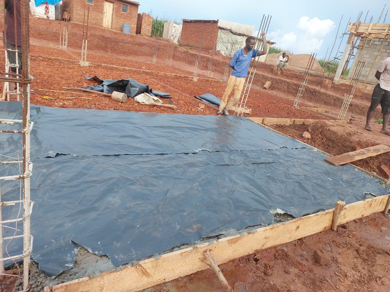 Slab curing. A freshly cast concrete slab was covered with polythene sheeting to retain moisture and cure properly, while formwork remained fixed at the edges to hold the slab in shape.