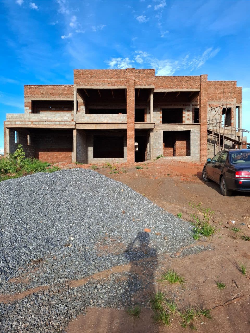 wall construction to roof level. Two-storey brick and block walls were completed up to wall-plate/roof level, with columns, lintel bands, and window and door openings clearly formed. The structure is now ready for roofing works to begin.